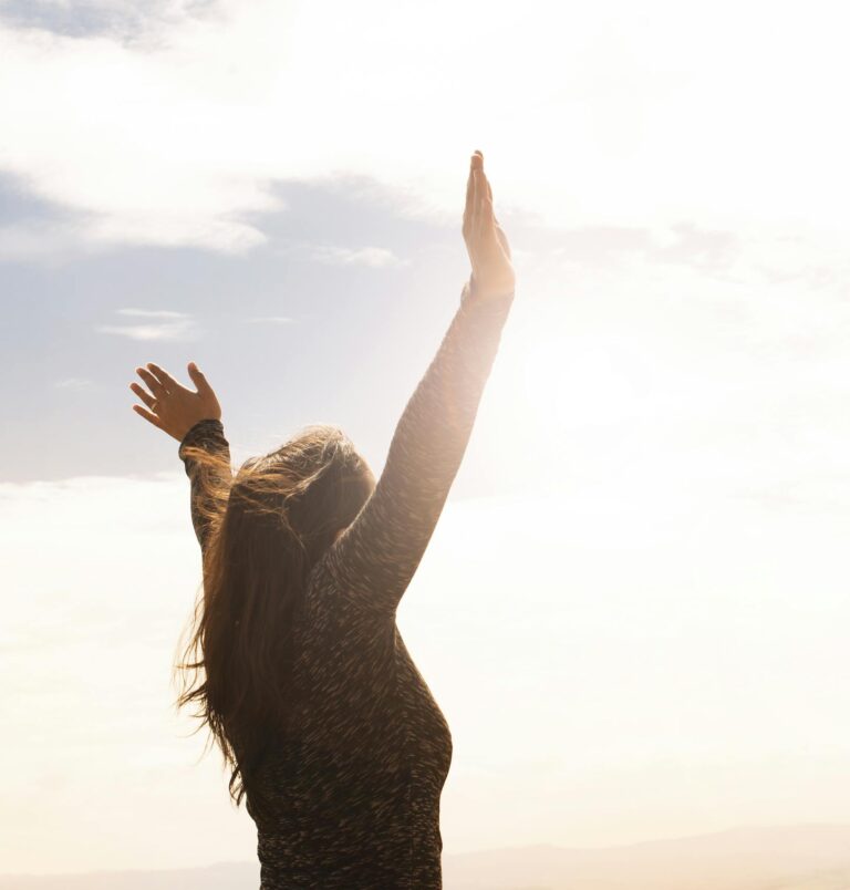 A woman with raised arms enjoying the bright open sky in a serene outdoor setting.